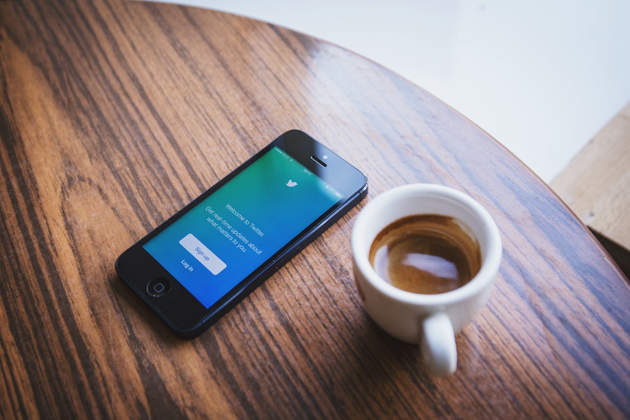 Close-up of a smartphone with the Twitter app next to a cup of coffee on a wooden table.